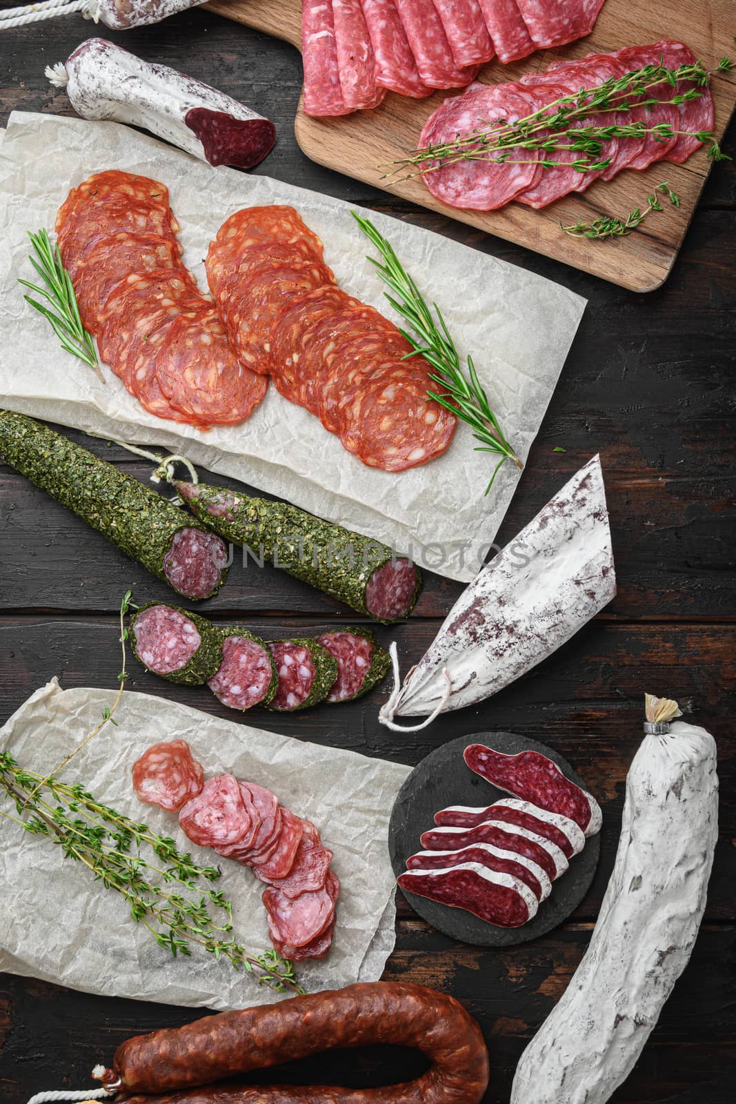 Variety of dry cured chorizo, fuet and other sausages cut in slices with herbs on dark wooden background, topview.