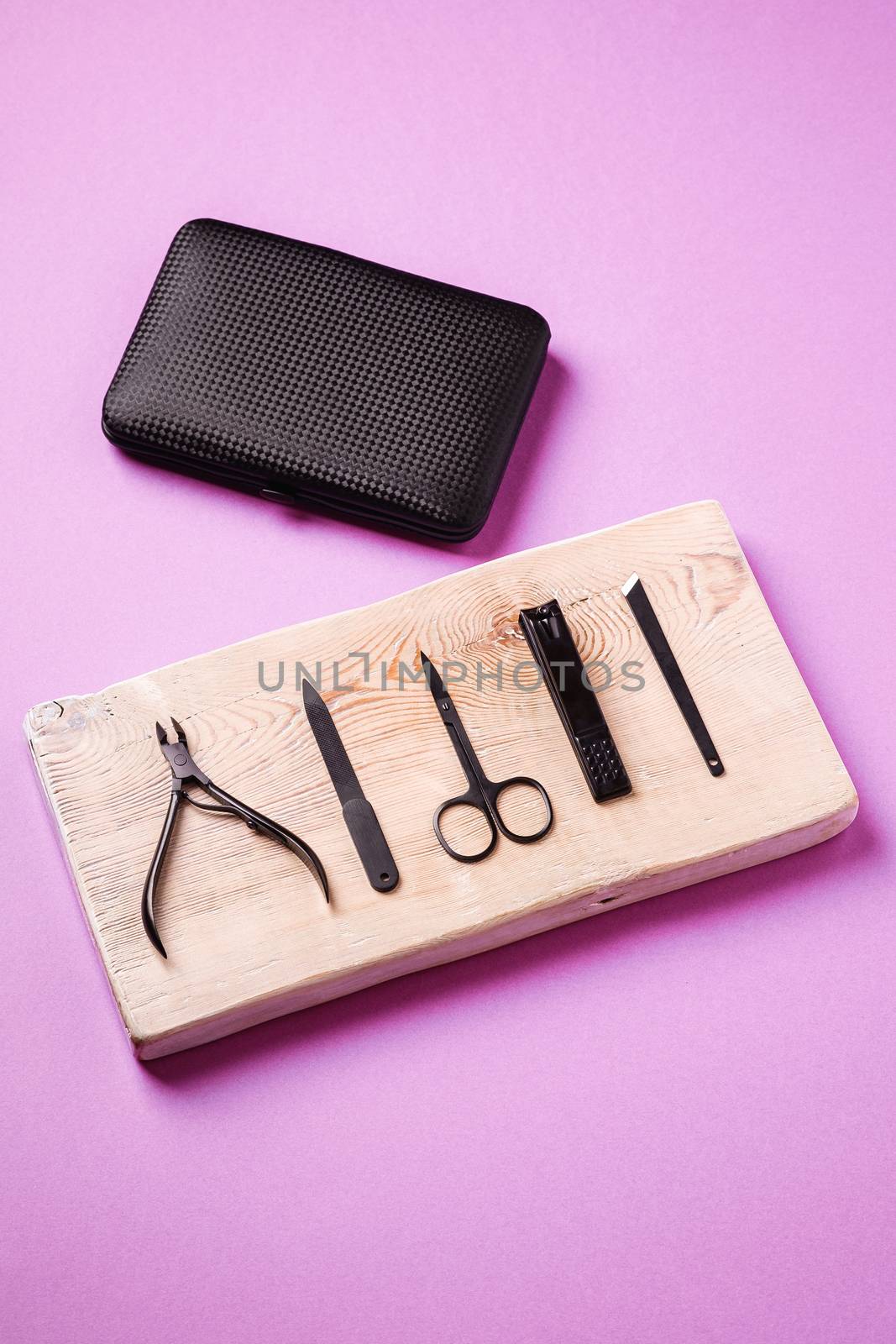 Set of manicure and pedicure tools and accessories on wooden board near to black case, angle view, pink background