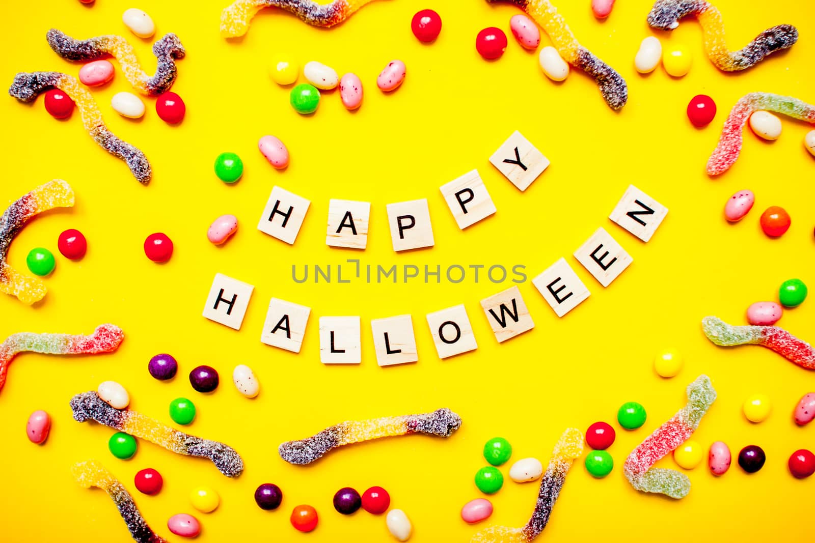 inscription from wooden blocks Happy Halloween and frame of multicolored candies and worms from gummy by malyshkamju