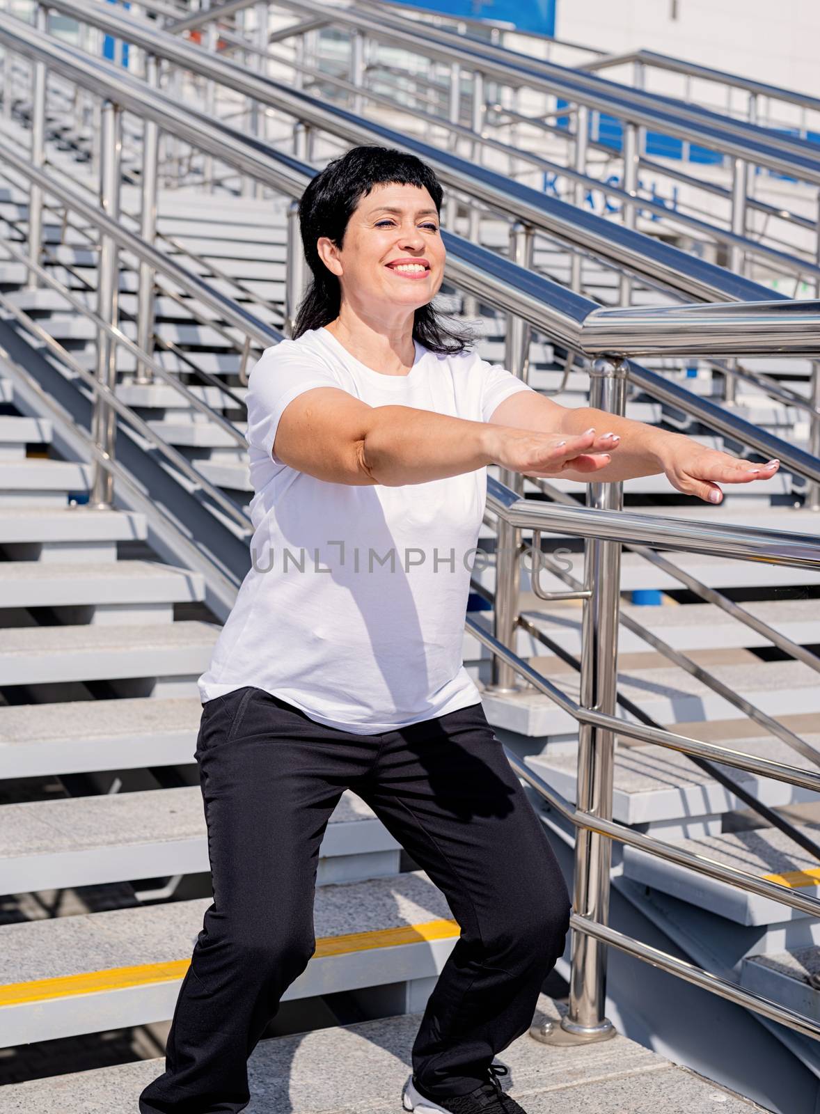 Smiling senior woman squatting outdoors on urban background by Desperada