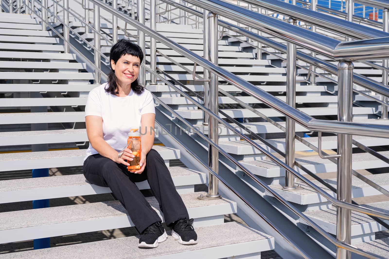 Sport and fitness. Senior sport. Active seniors. Smiling senior woman drinking water after workout outdoors on urban background