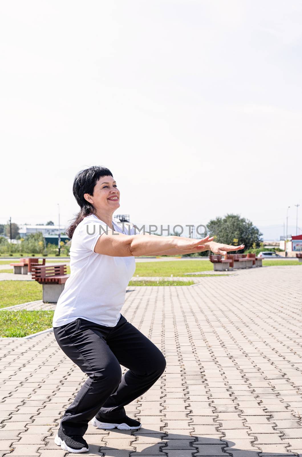 Smiling senior woman squatting outdoors in the park by Desperada