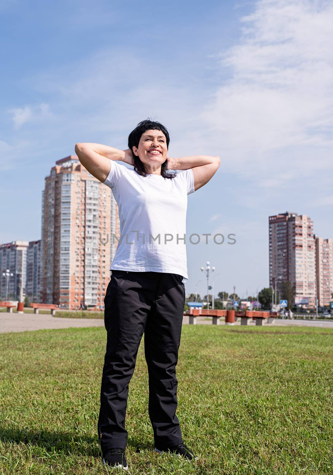 Sport and fitness. Senior sport. Active seniors. Smiling senior woman warming up before training outdoors in the park on urban background