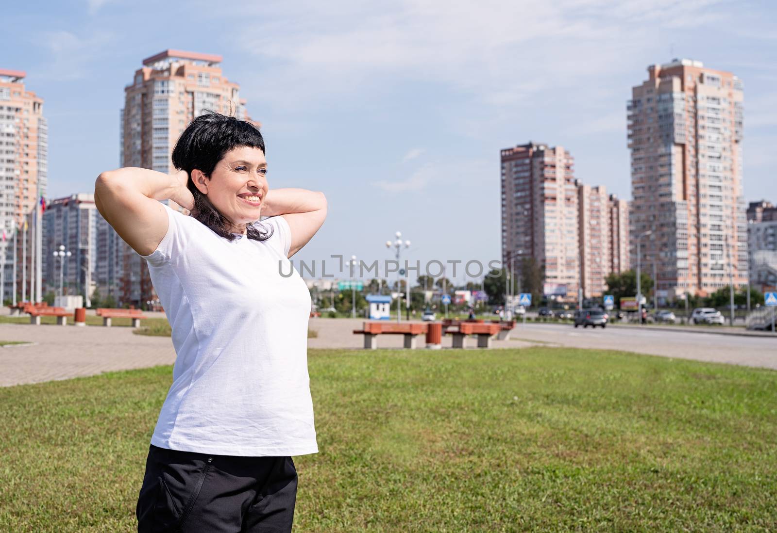 Sport and fitness. Senior sport. Active seniors. Smiling senior woman warming up before training outdoors in the park on urban background