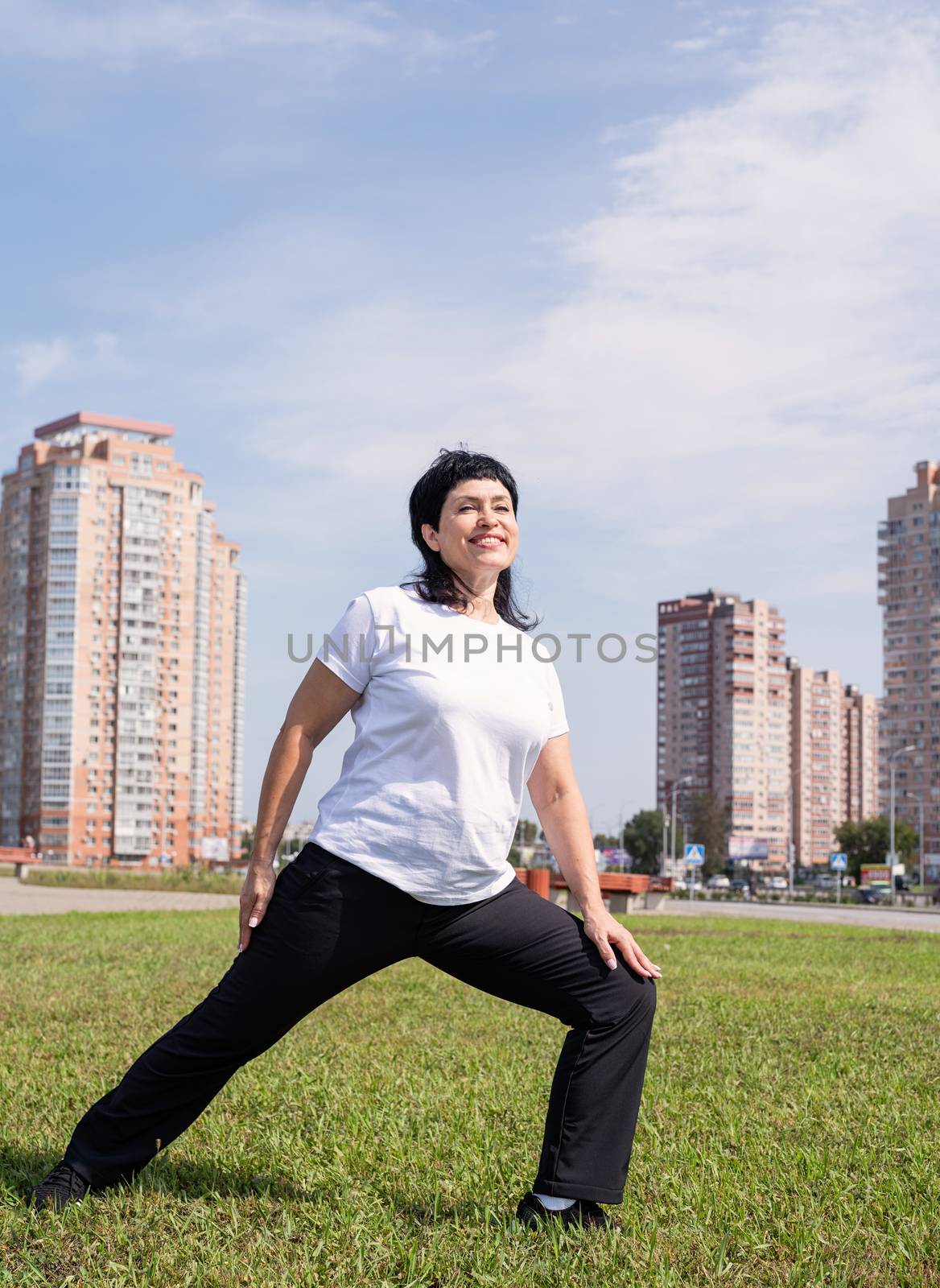 Smiling senior woman warming up stretching outdoors in the park by Desperada