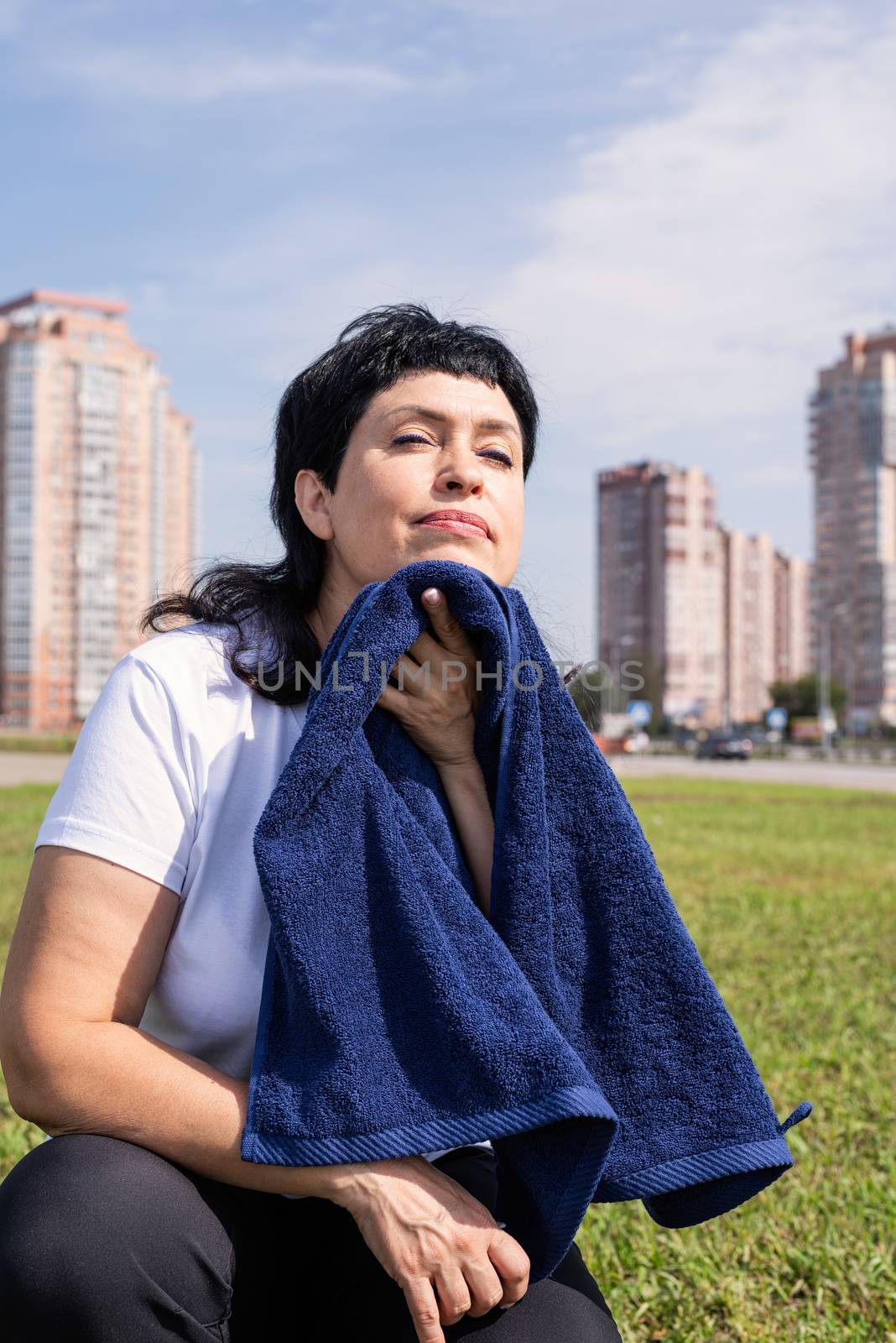 senior woman wiping out sweat after hard workout outdoors in the park by Desperada