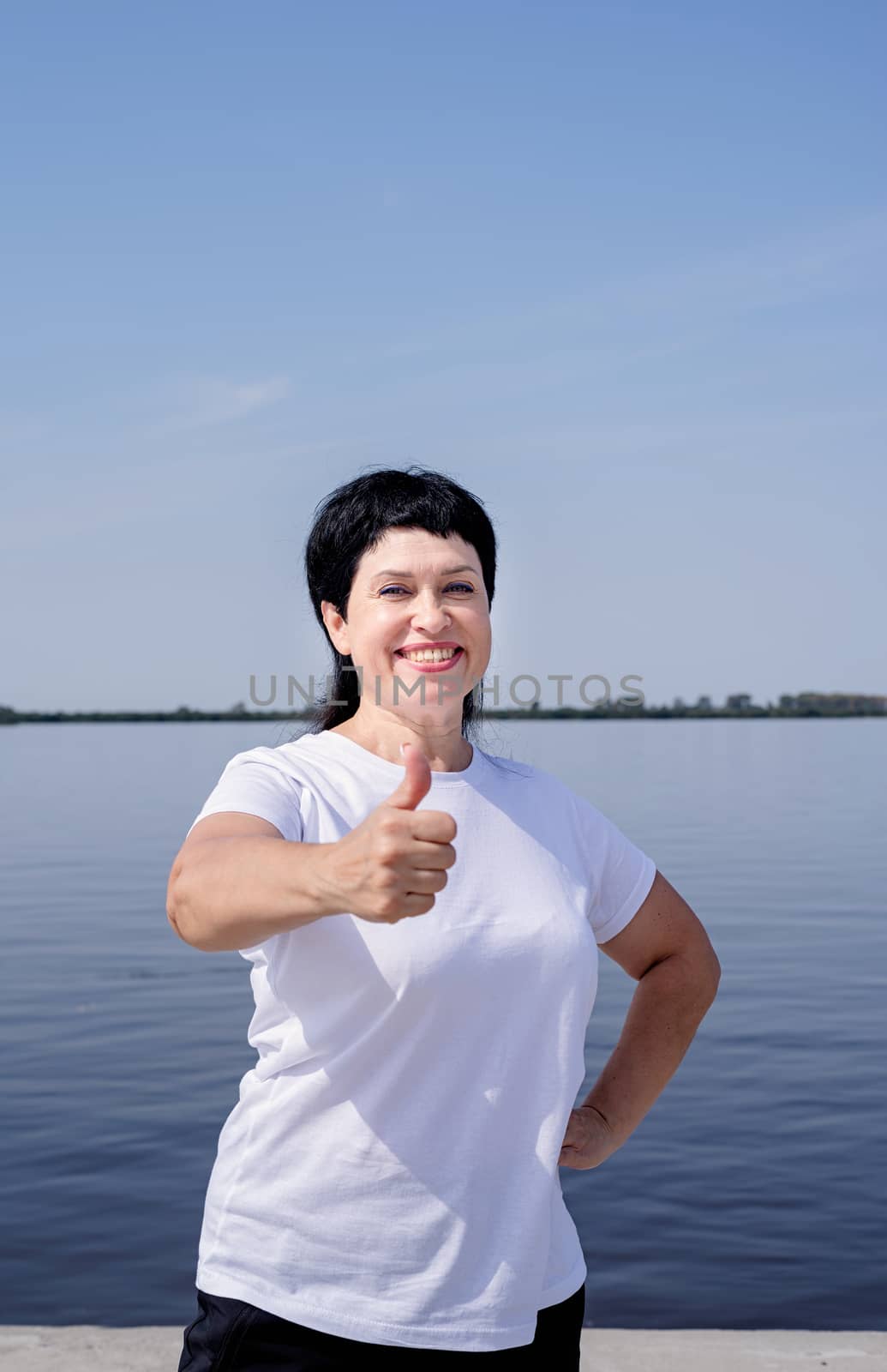 Sport and fitness. Senior sport. Active seniors. Active and happy senior woman in sportswear showing thumbs up working out near the riverside