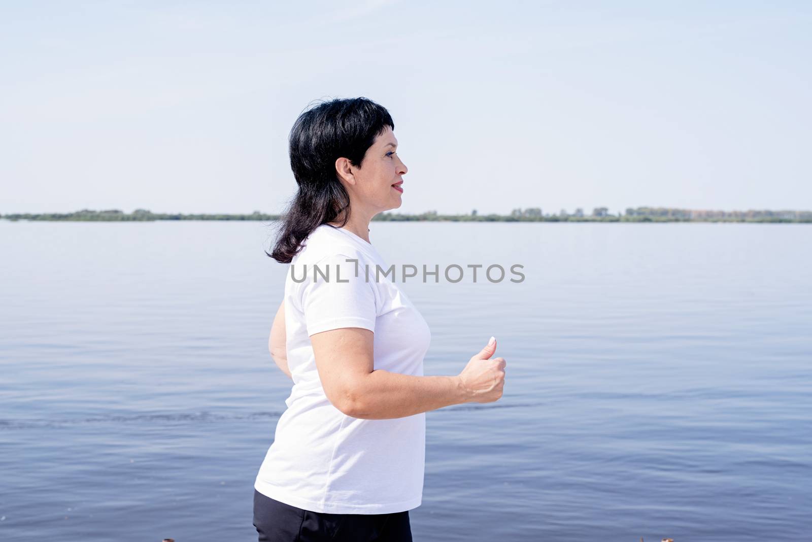 Sport and fitness. Senior sport. Active seniors. Active senior woman jogging near the riverside