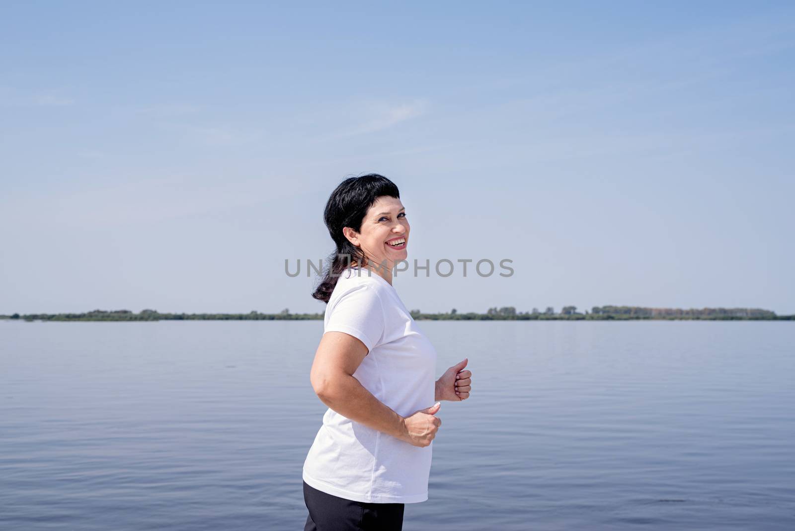 Active laughing senior woman jogging near the riverside by Desperada