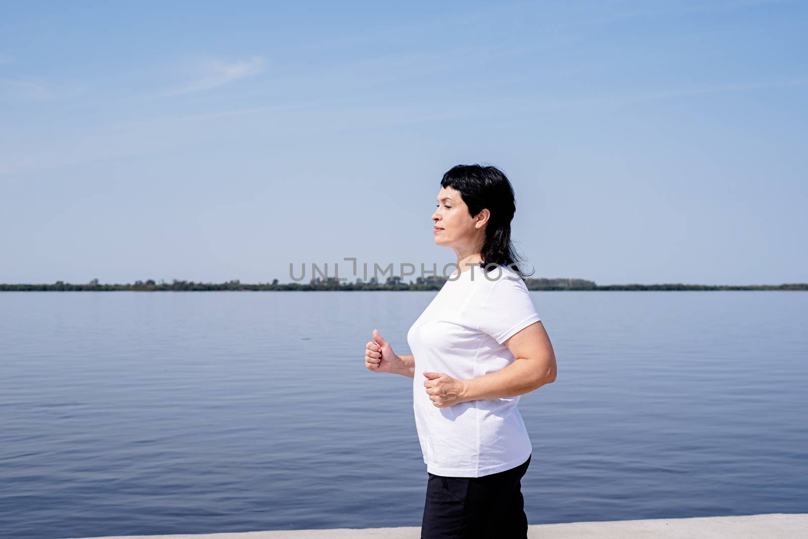 Active senior woman jogging near the riverside by Desperada