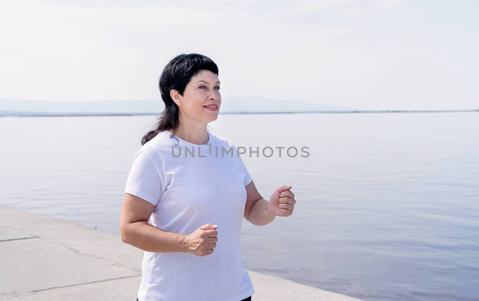 Sport and fitness. Senior sport. Active seniors. Active senior woman jogging near the riverside