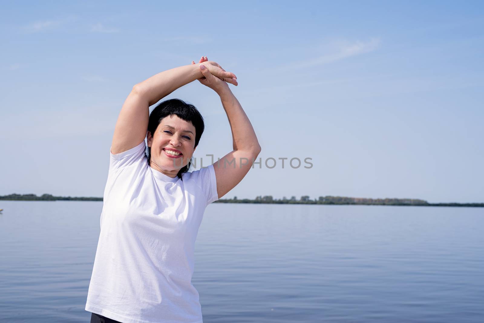 Sport and fitness. Senior sport. Active seniors. Active and happy senior woman doing stretching near the riverside