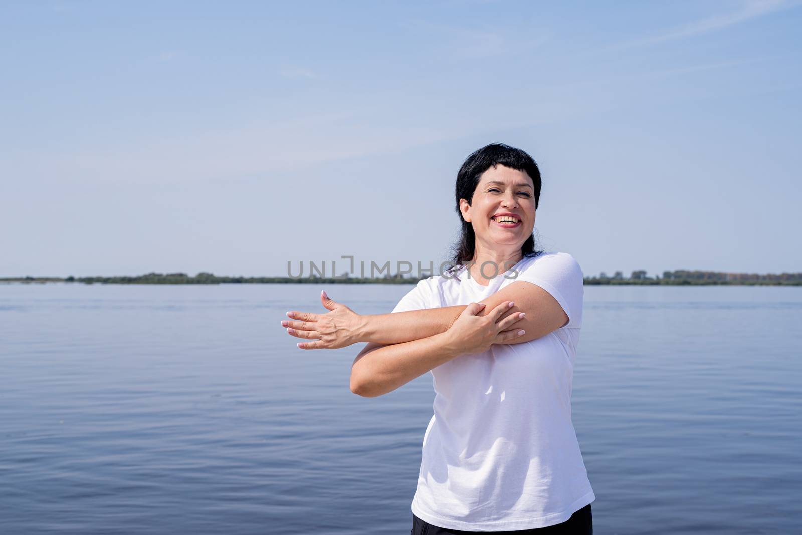 Active and happy senior woman doing stretching near the riverside by Desperada