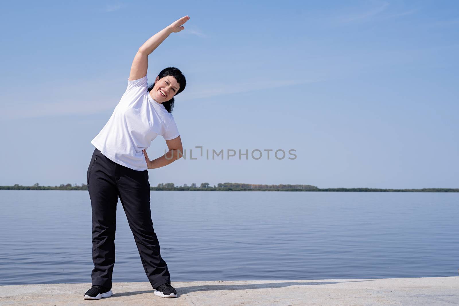 Sport and fitness. Senior sport. Active seniors. Active and happy senior woman doing stretching near the riverside