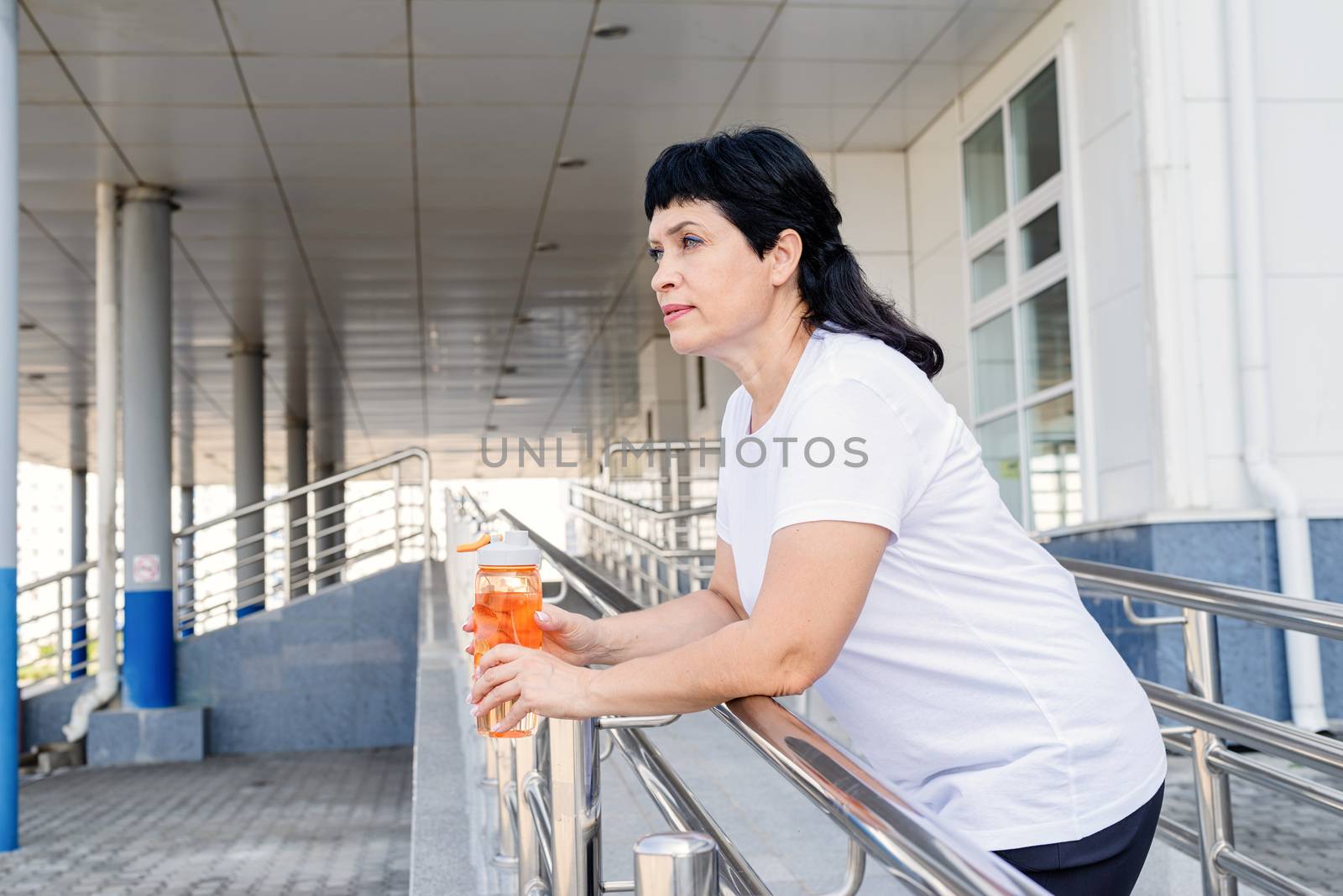 senior woman drinking water after workout outdoors on urban background by Desperada