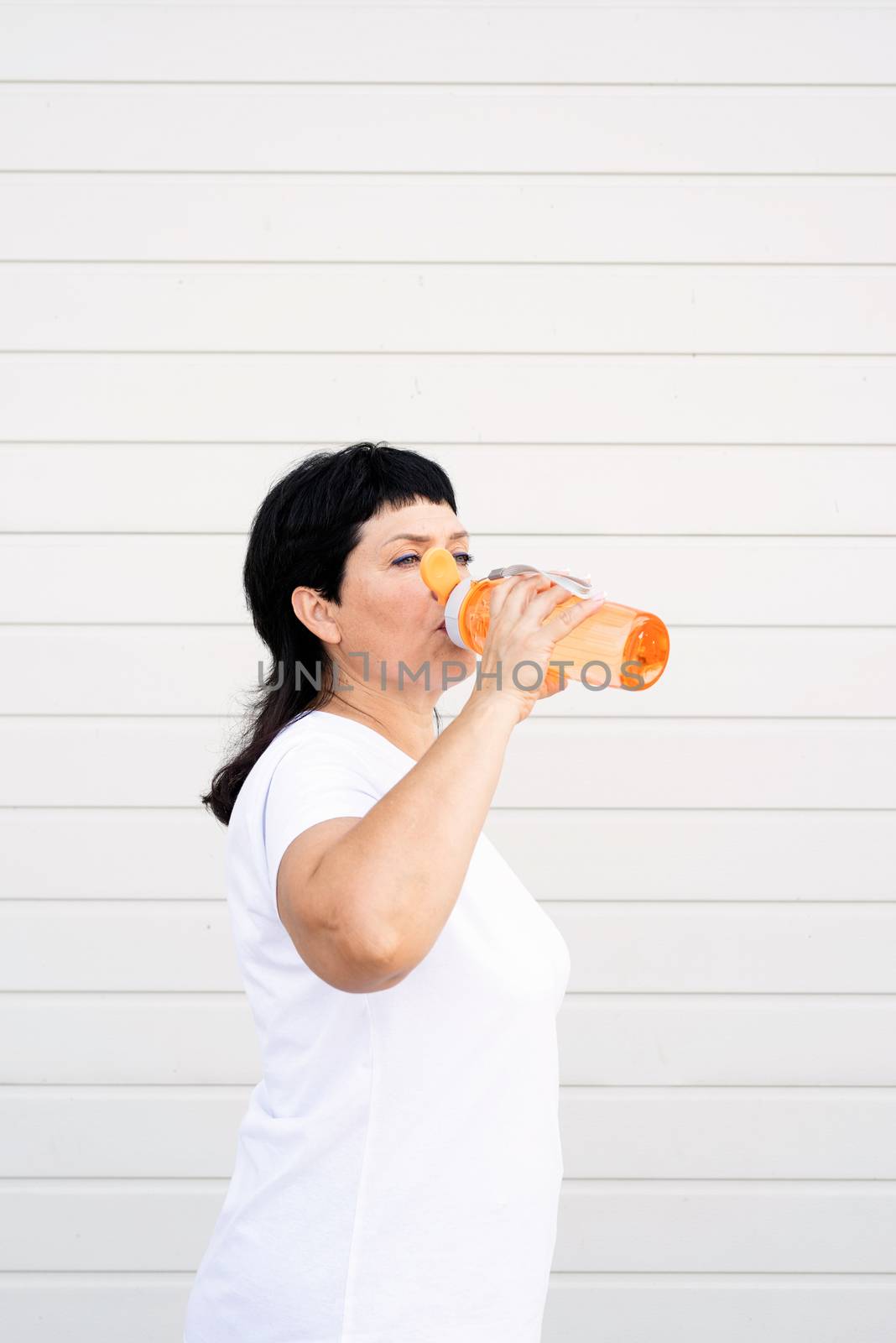 Sport and fitness. Senior sport. Active seniors. Smiling senior woman drinking water after workout outdoors on urban background