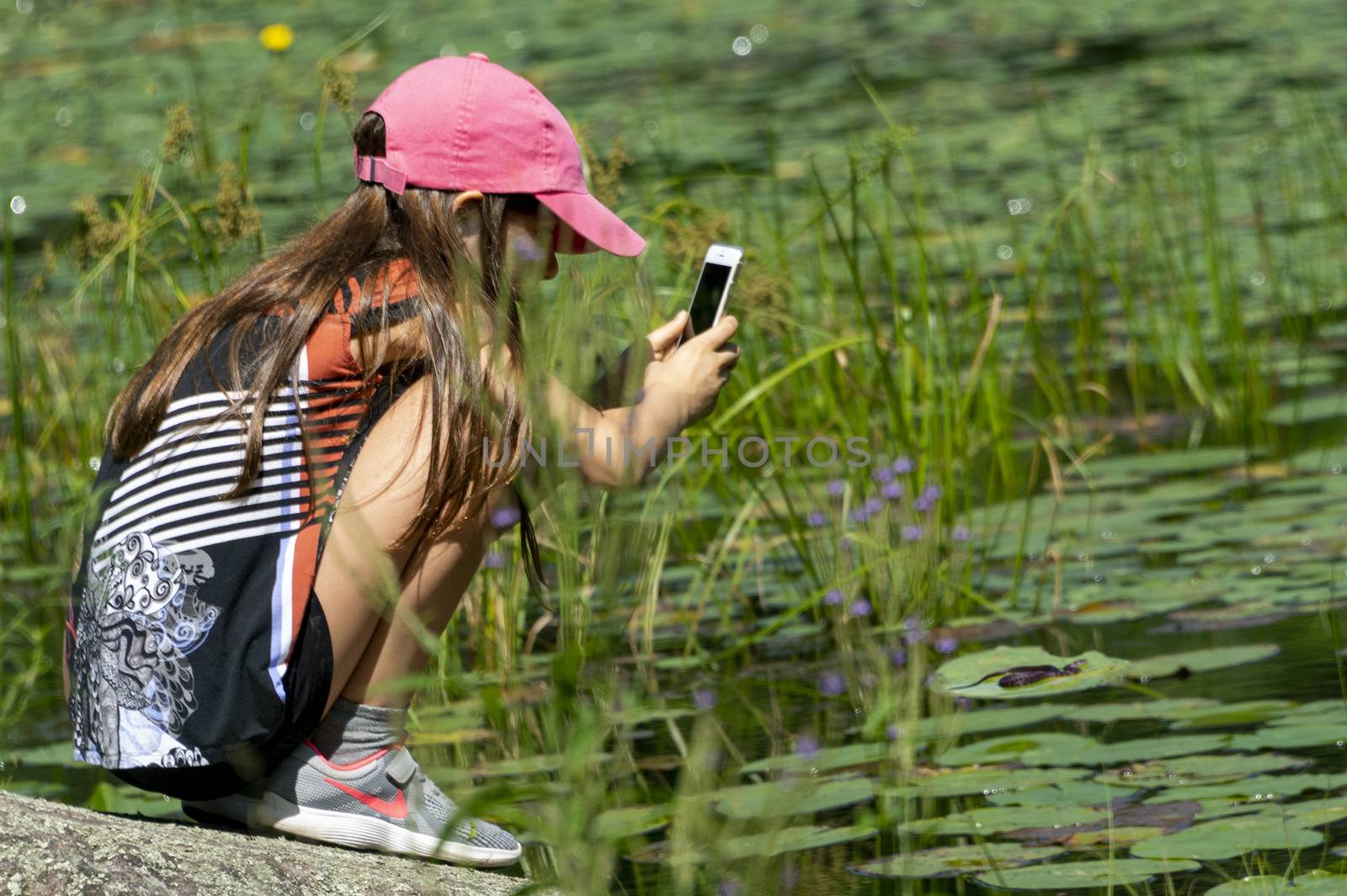 The girl saw a snake on the lake and is trying to photograph it