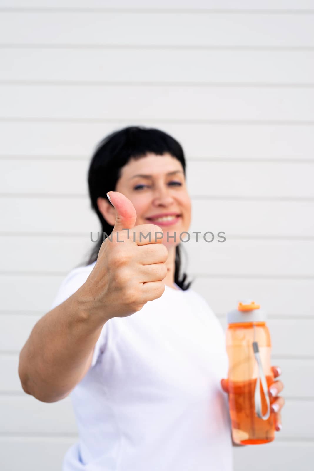Sport and fitness. Senior sport. Active seniors. Smiling senior woman showing thumbs up after standing outdoors on gray solid background