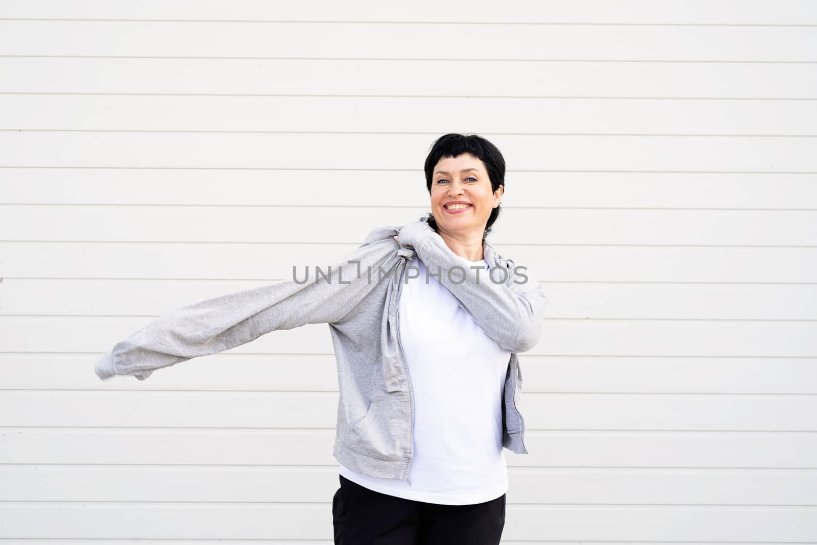 Sport and fitness. Senior sport. Active seniors. Senior woman waring gray jacket standing outdoors on gray solid background