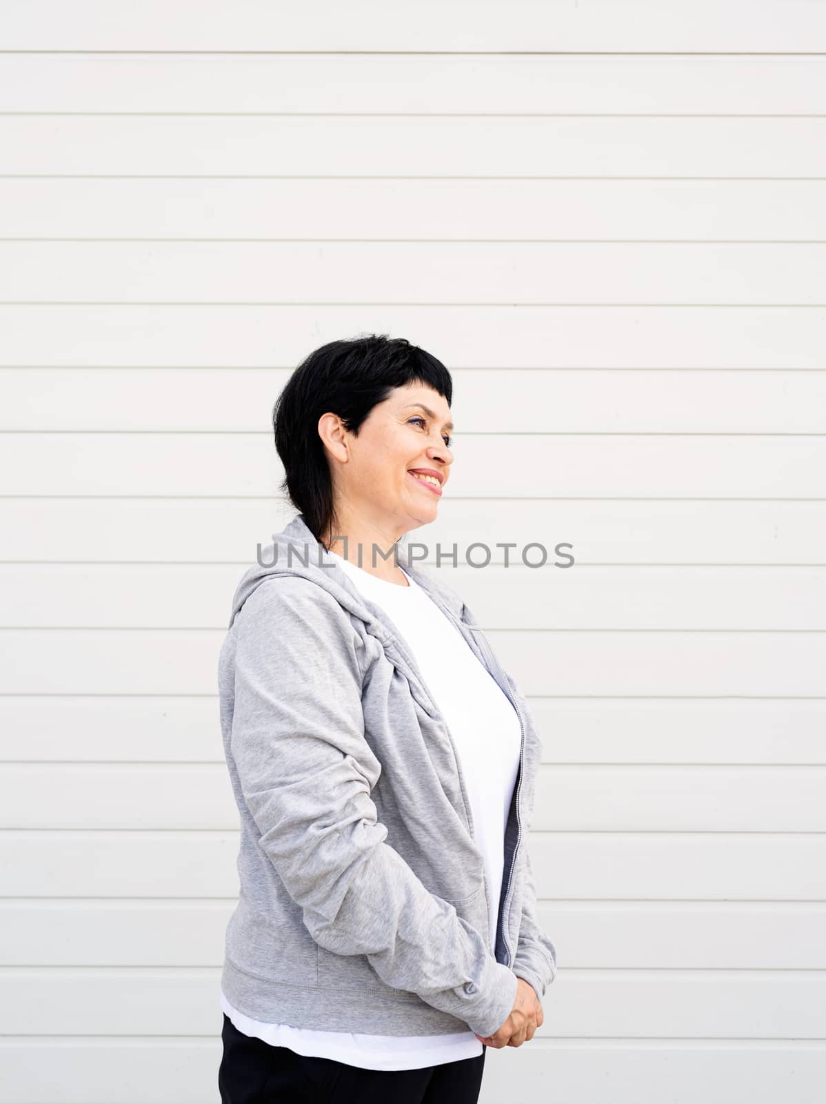 Senior woman waring gray jacket standing outdoors on gray solid background by Desperada