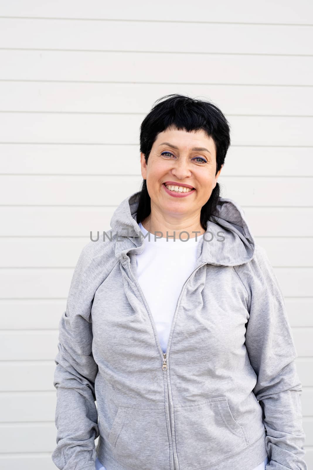 Sport and fitness. Senior sport. Active seniors. Senior woman waring gray jacket standing outdoors on gray solid background