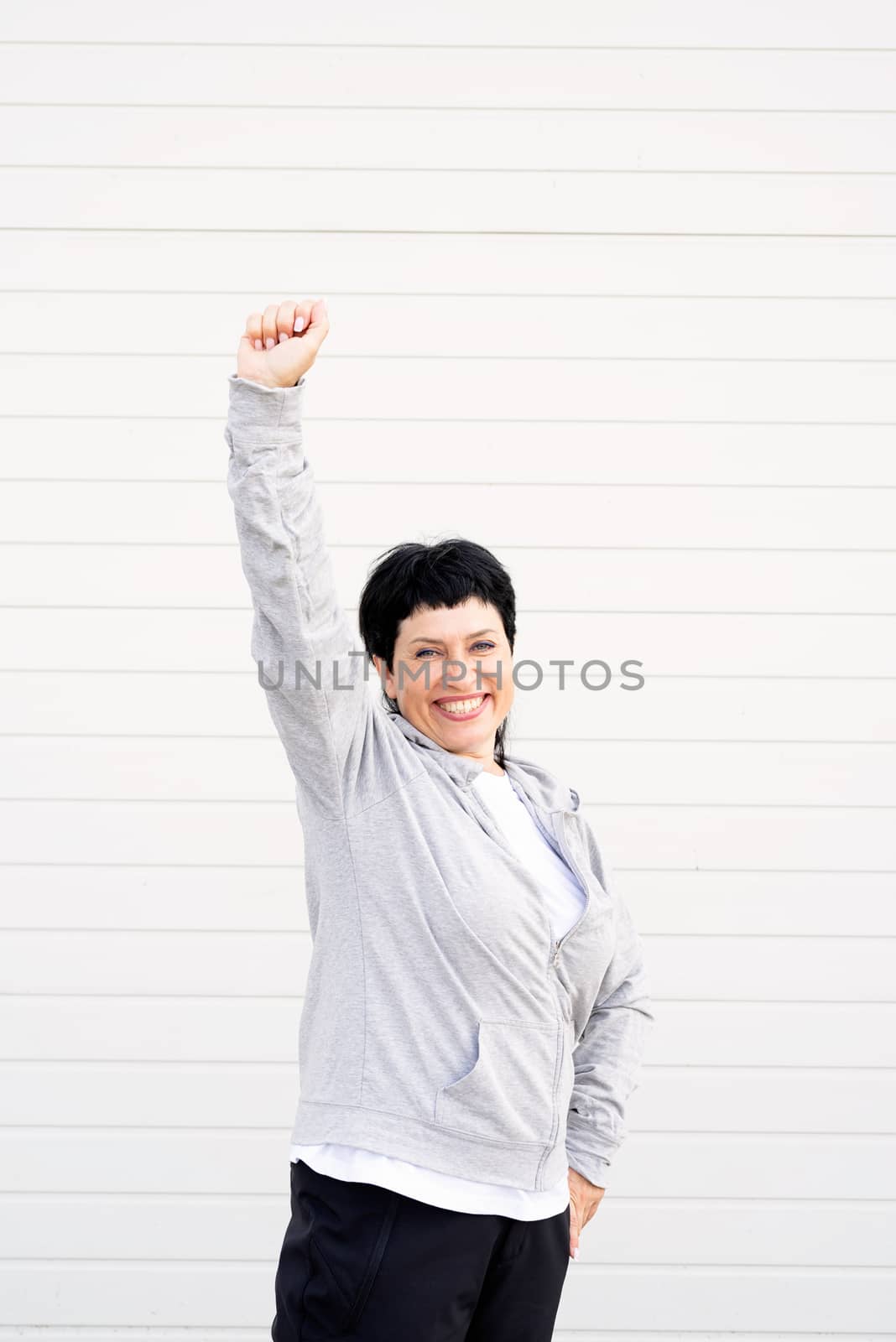 Sport and fitness. Senior sport. Active seniors. happy senior woman standing outdoors on gray solid background with arms up