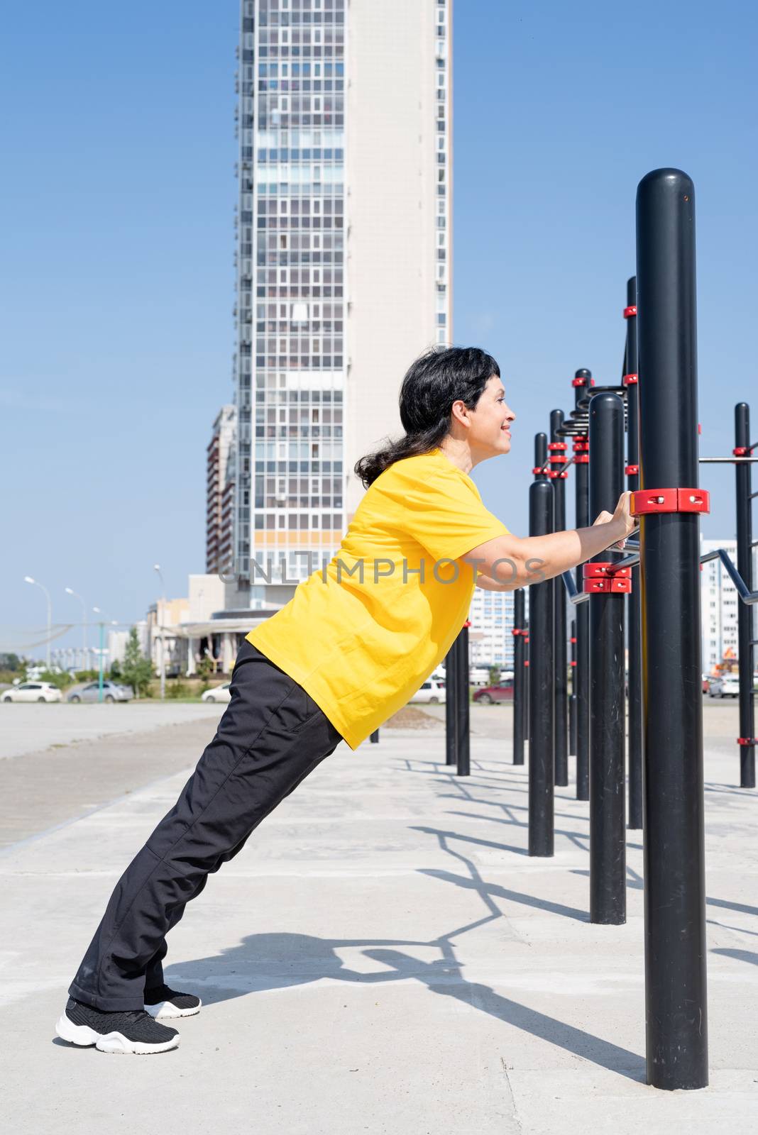 Smiling senior woman doing push ups outdoors on the sports ground bars by Desperada