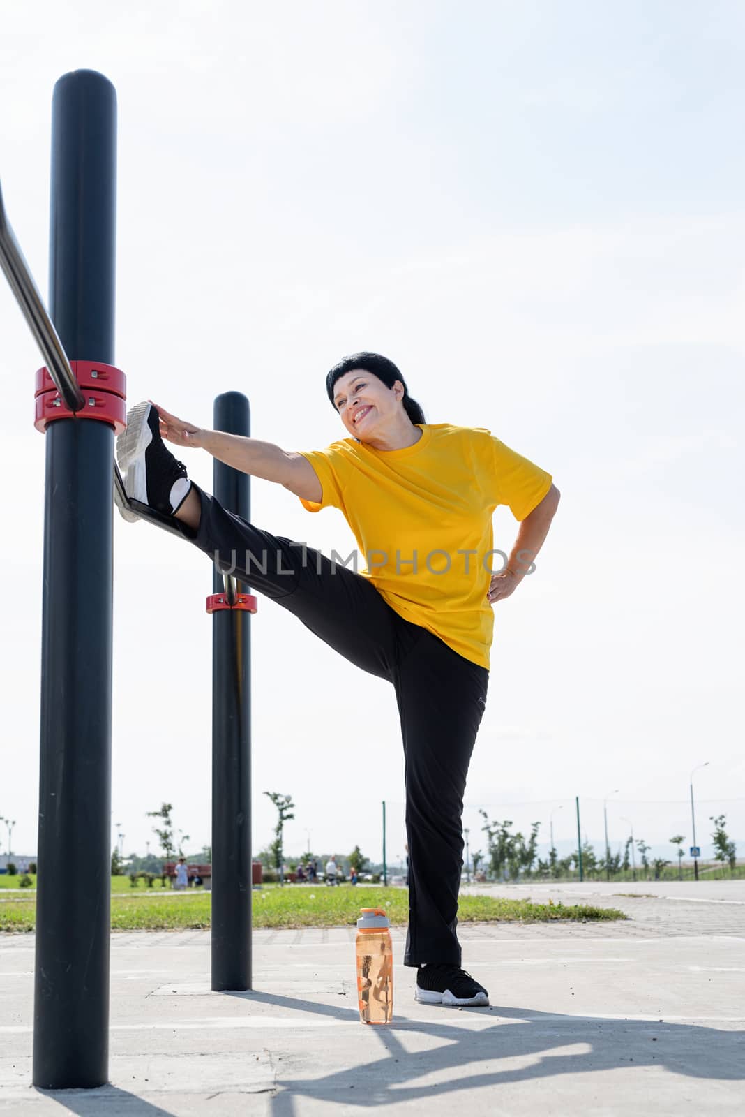 Senior woman stretching her legs outdoors on the sports ground by Desperada