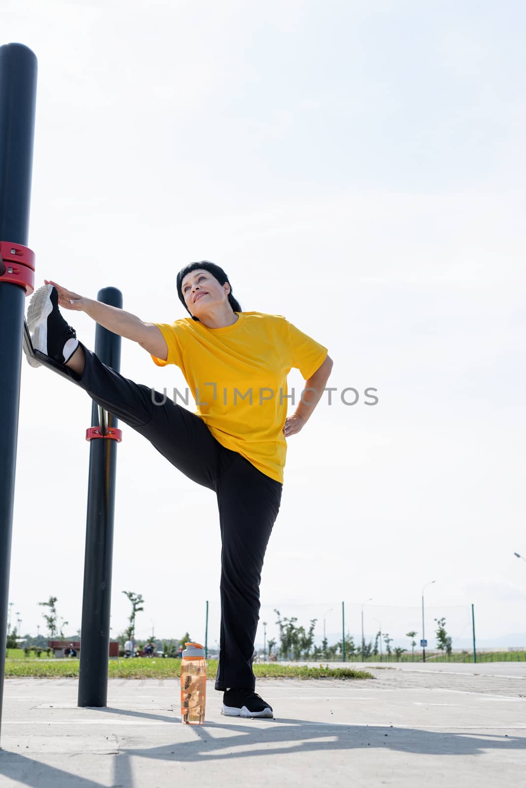 Sport and fitness. Senior sport. Active seniors. Senior woman stretching her legs outdoors on the sports ground