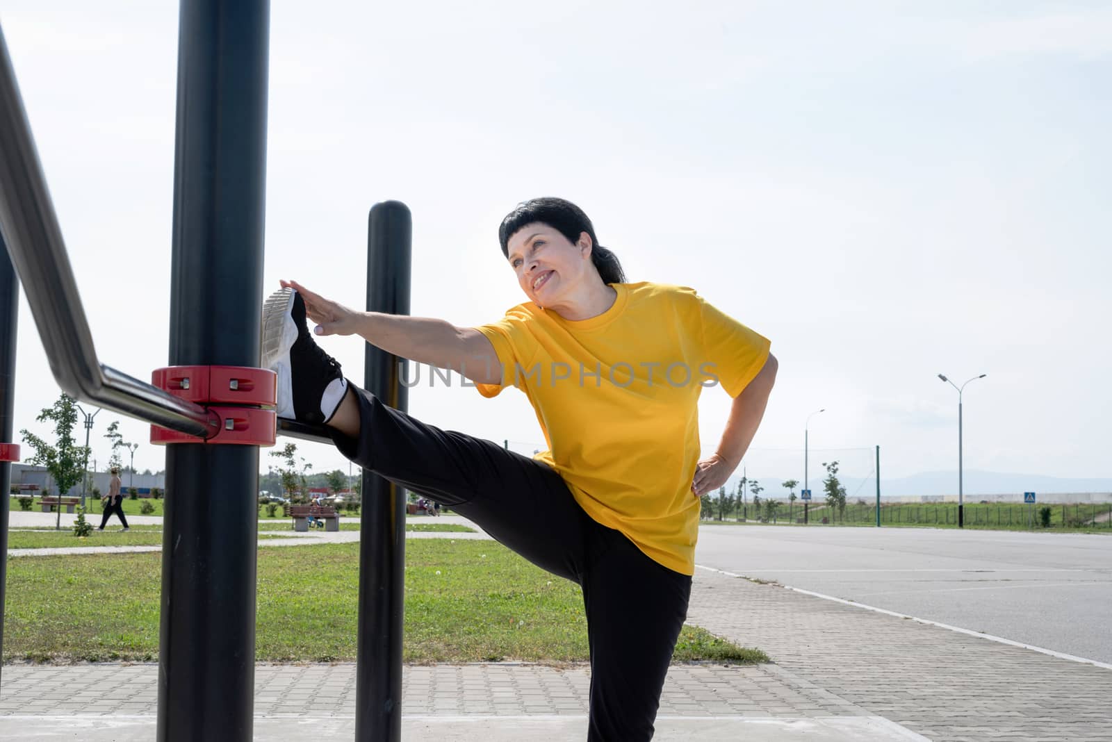 Senior woman stretching her legs outdoors on the sports ground by Desperada