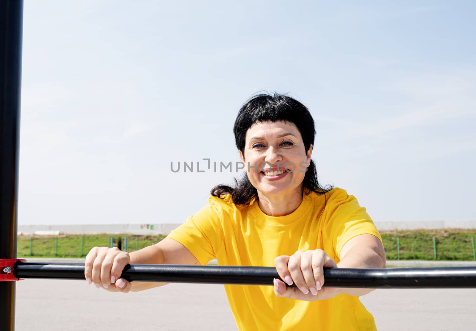 Smiling senior woman doing push-ups outdoors by Desperada