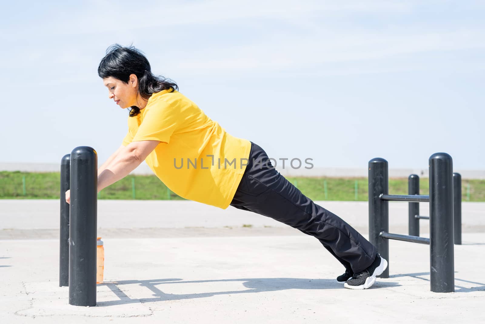 Smiling senior woman doing push ups outdoors on the sports ground bars by Desperada