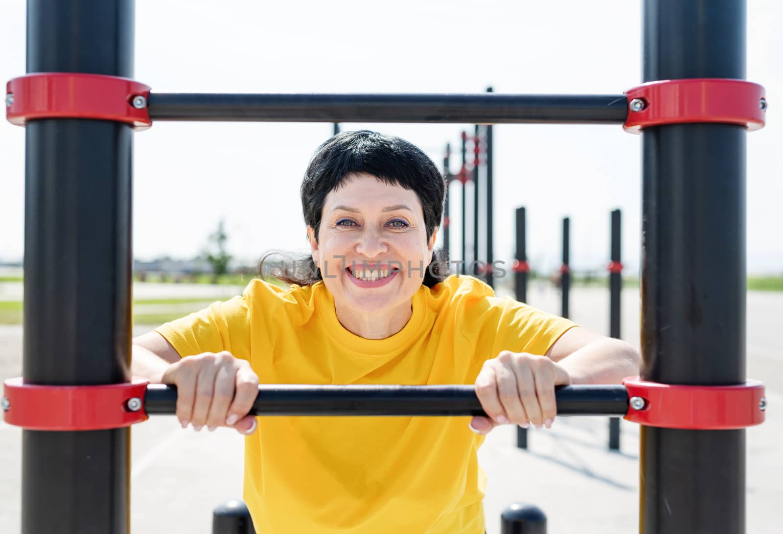 Smiling senior woman doing push-ups outdoors by Desperada