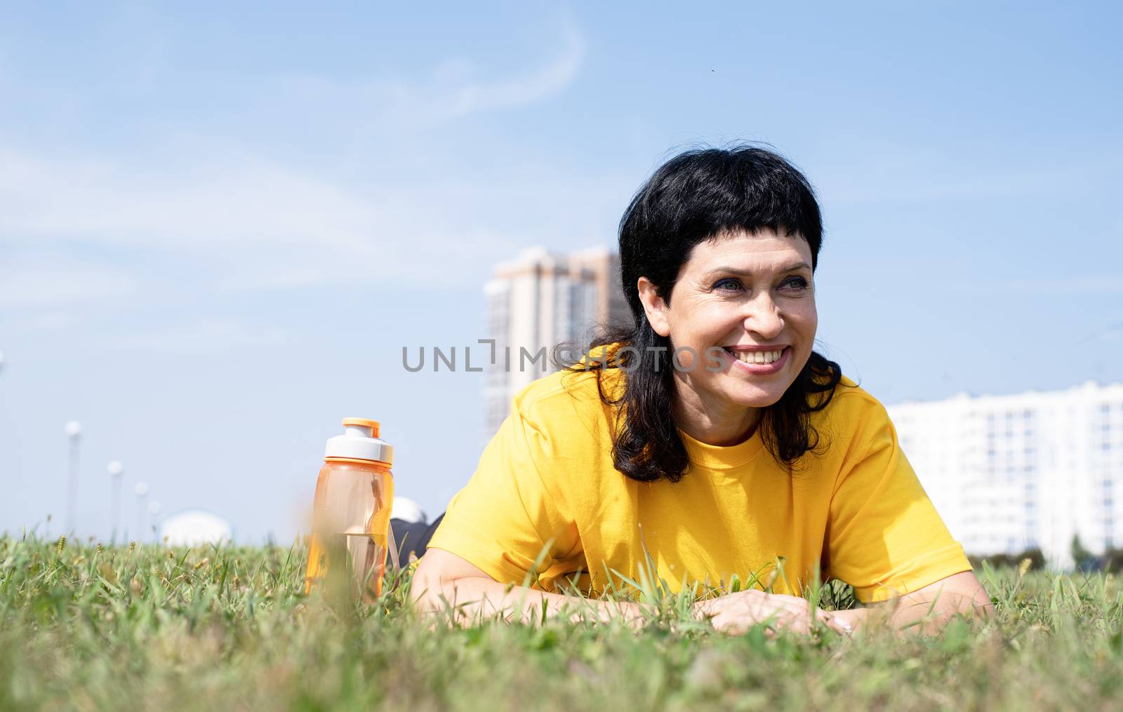 Sport and fitness. Senior sport. Active seniors. Senior woman laying on grass in the park on urban background