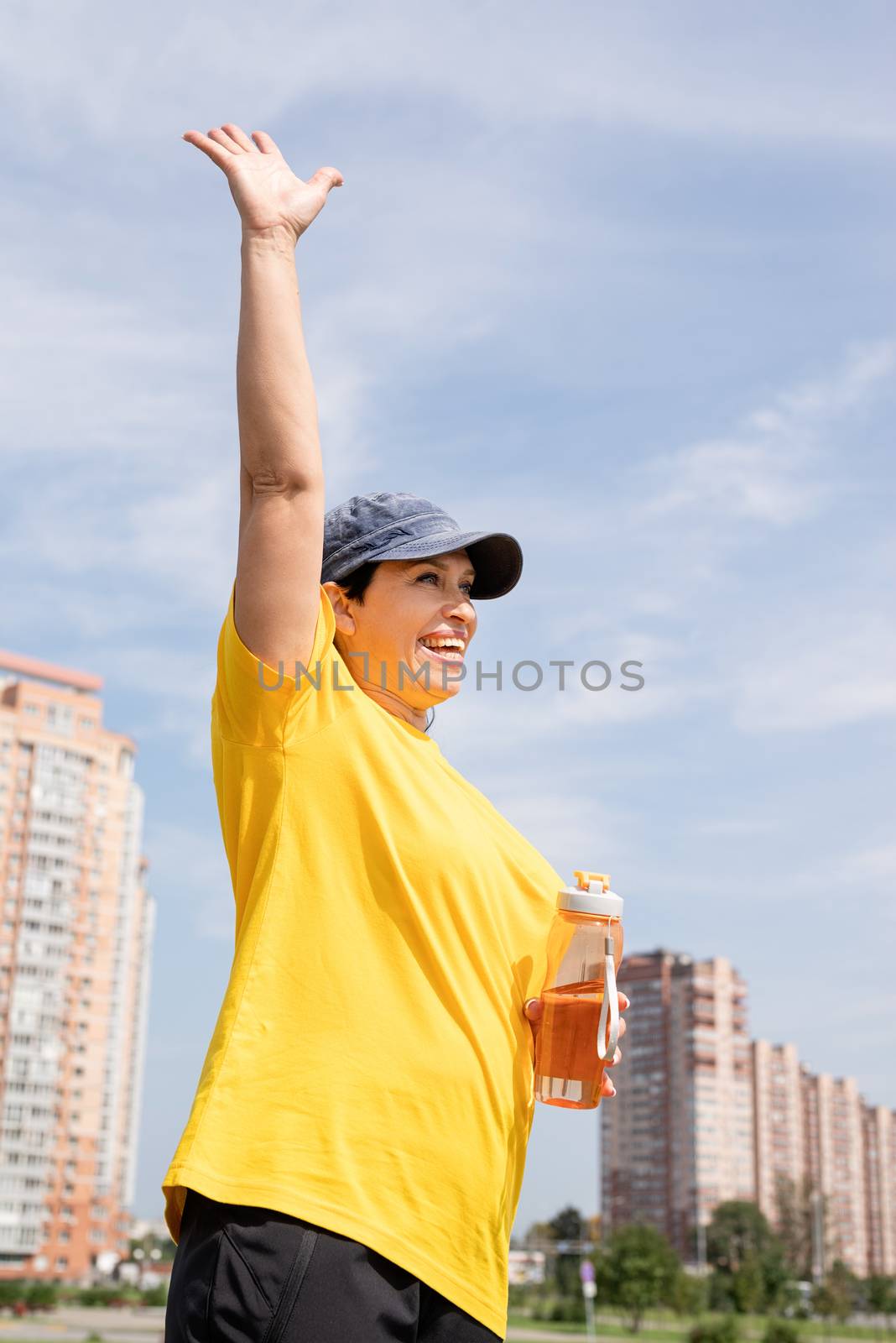 Sport and fitness. Senior sport. Active seniors. Excited senior woman saying hello drinking water after workout outdoors on the sports ground