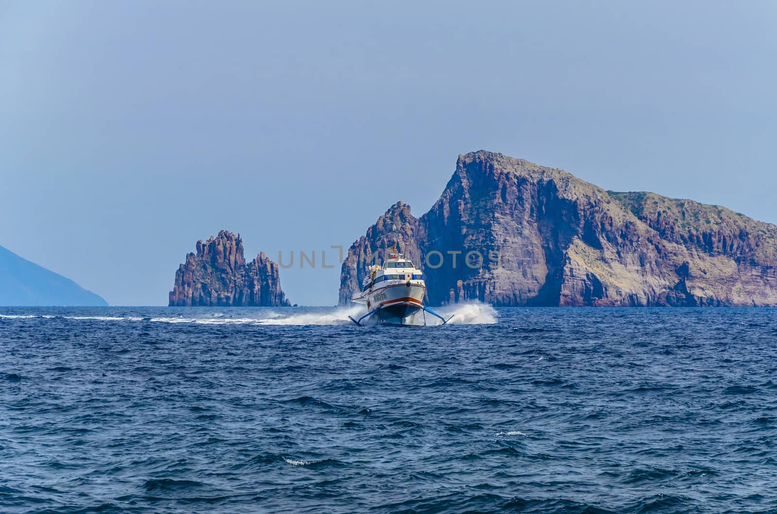 Ferry catamaran covering the route between the islands of Stromboli and Panarea in the Tyrrhenian Sea and two large cliffs behind it