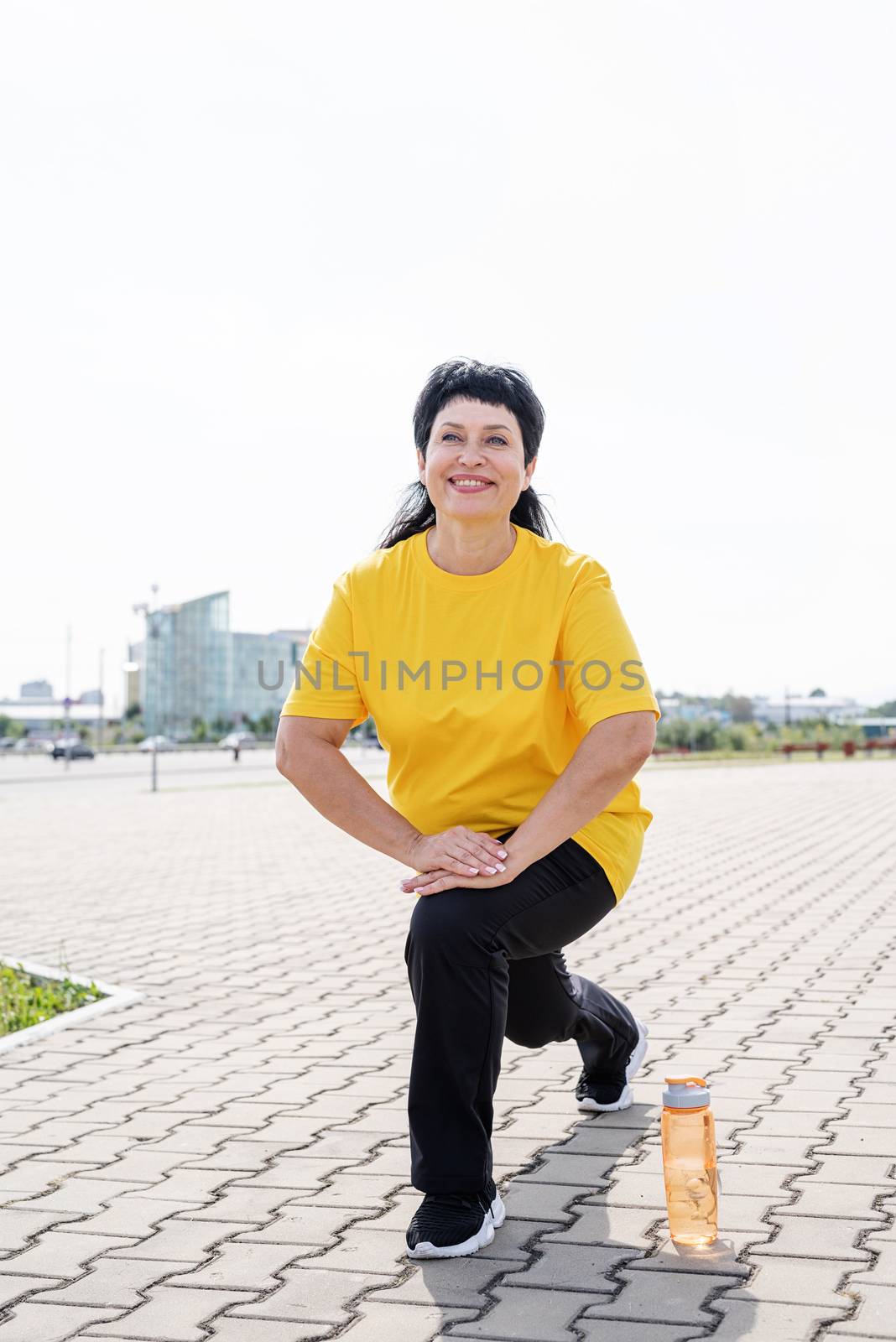 Smiling senior woman warming up stretching outdoors in the park by Desperada