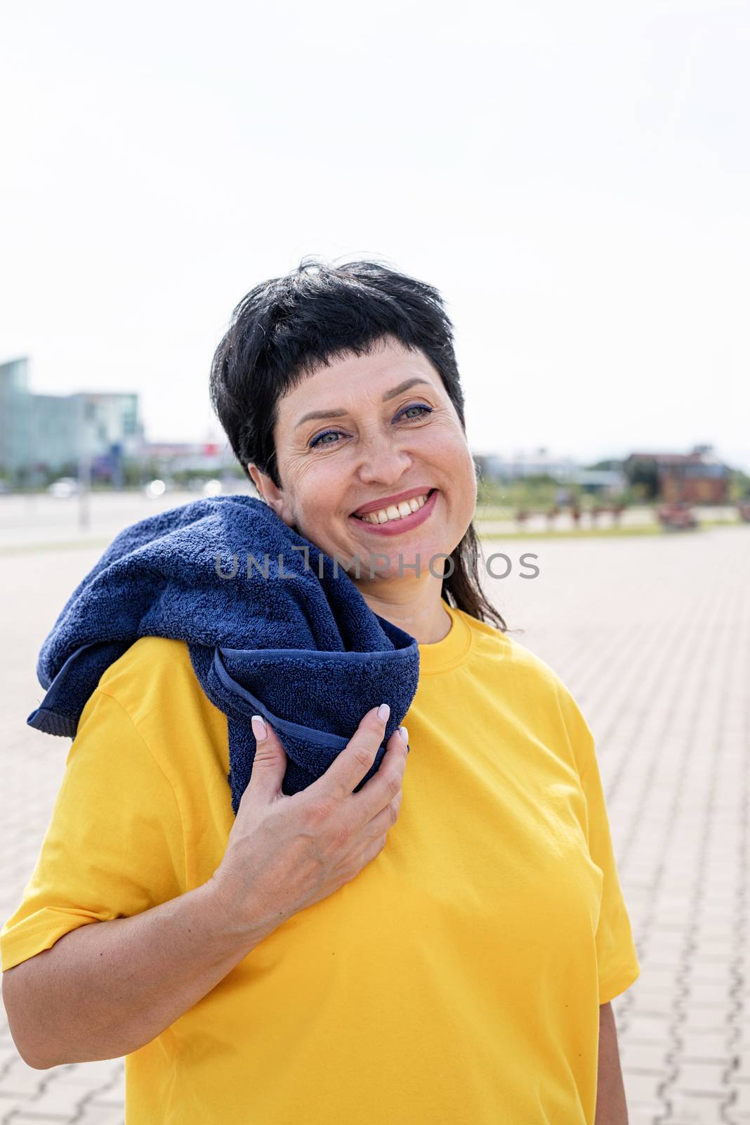 Smiling senior woman wiping out sweat after hard workout outdoors in the park by Desperada