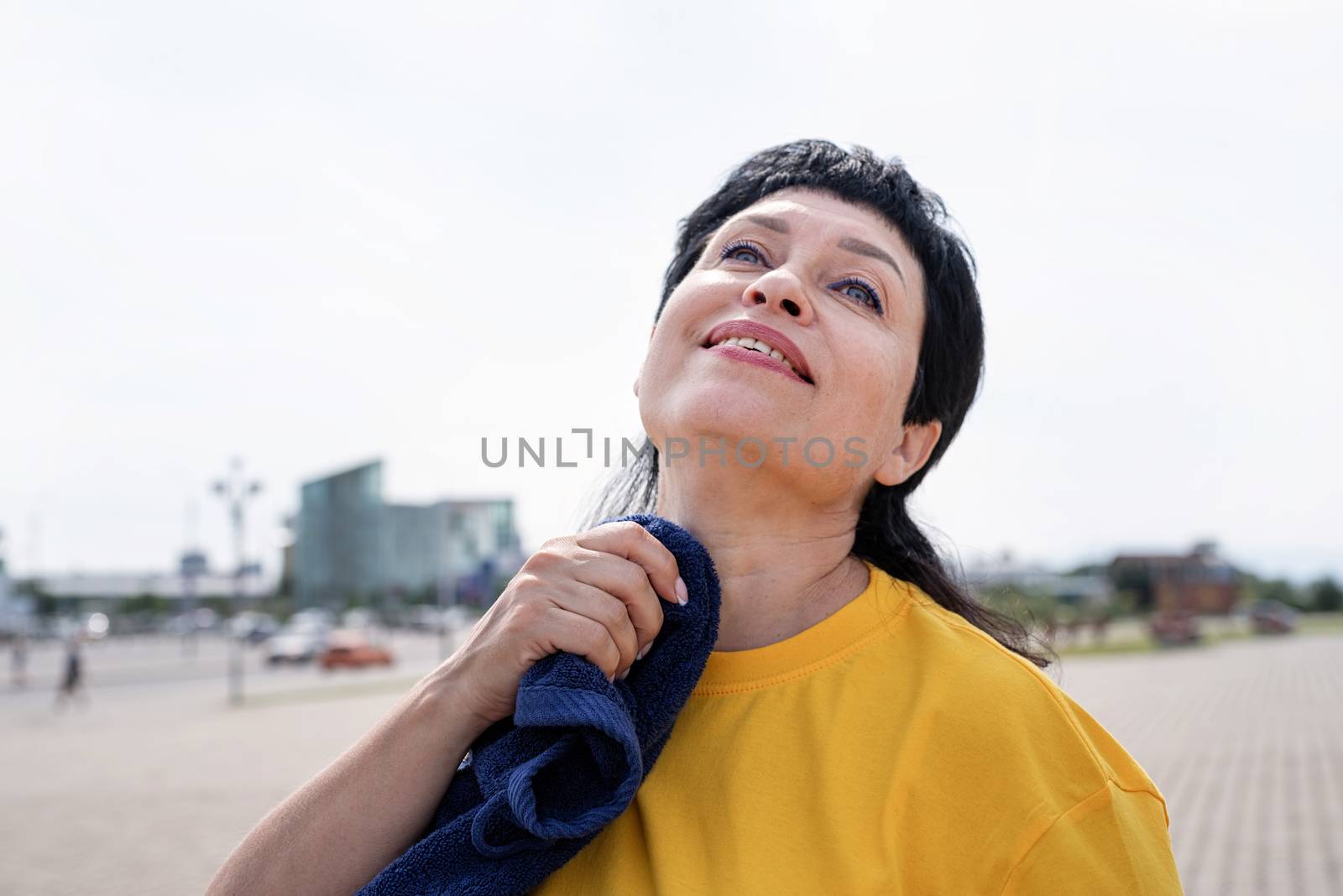 Smiling senior woman wiping out sweat after hard workout outdoors in the park by Desperada