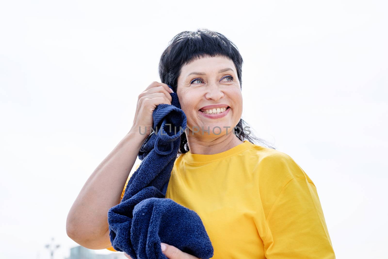 Smiling senior woman wiping out sweat after hard workout outdoors in the park by Desperada