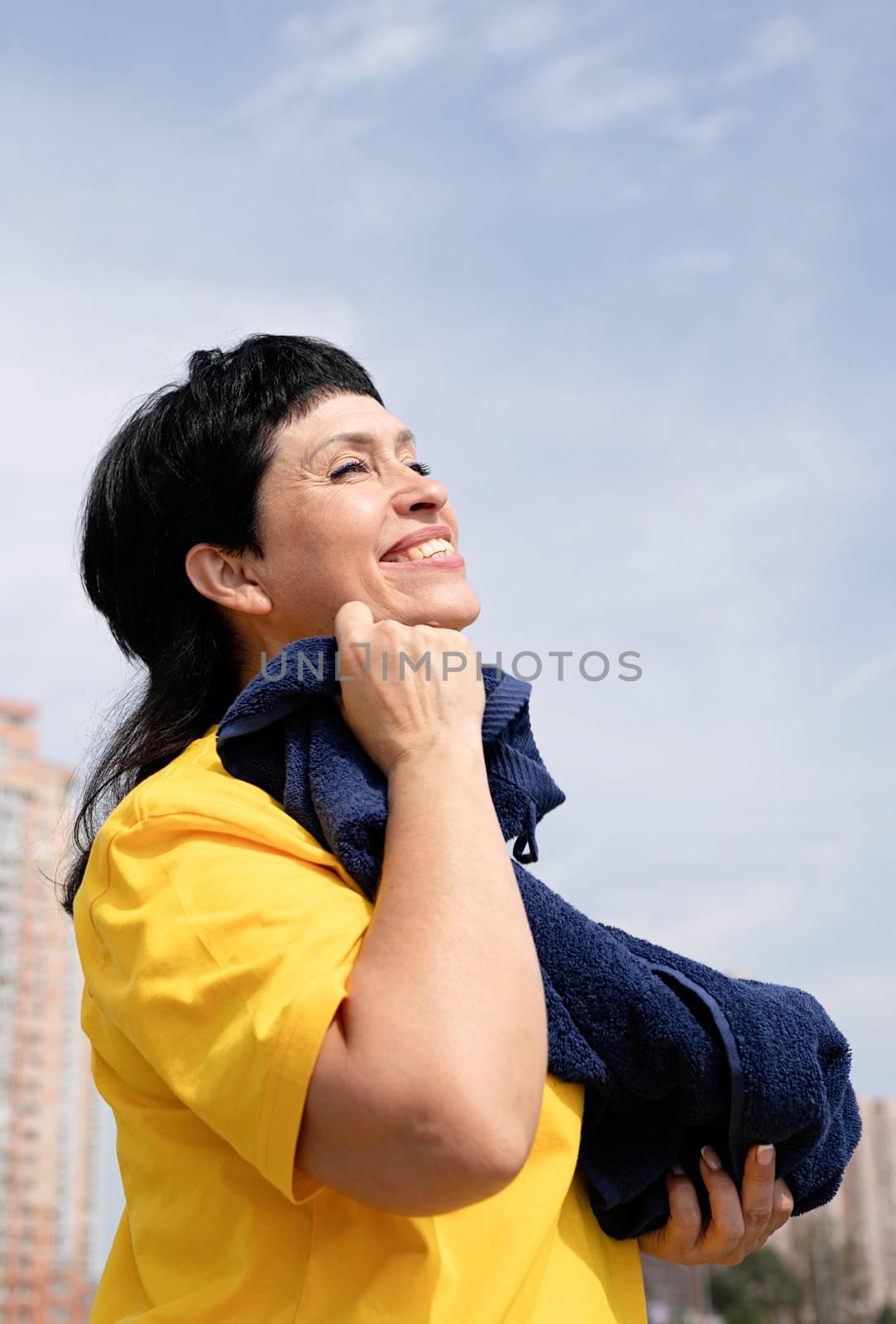 Smiling senior woman wiping out sweat after hard workout outdoors in the park by Desperada