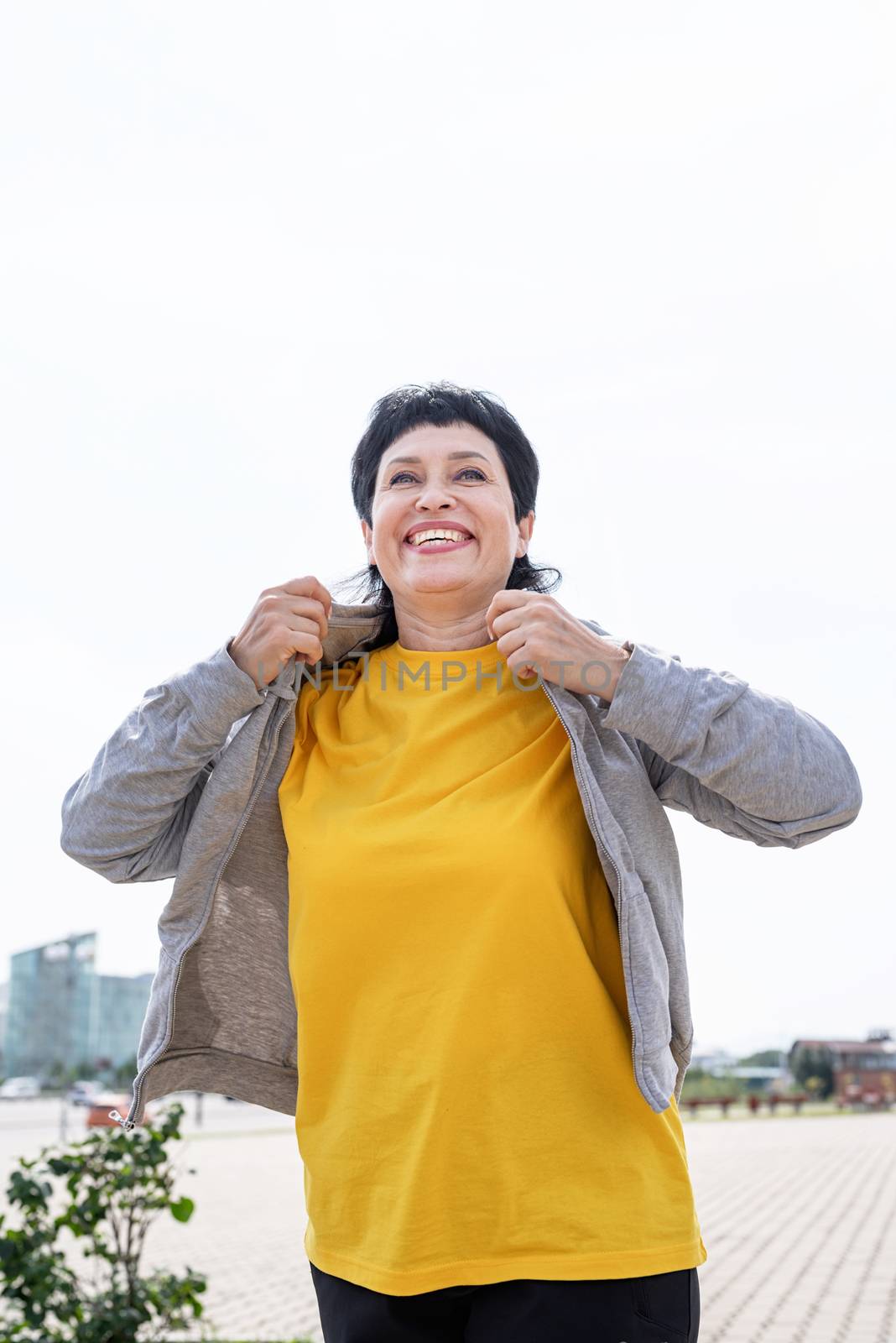 Sport and fitness. Senior sport. Active seniors. Senior woman waring gray jacket on the sports ground