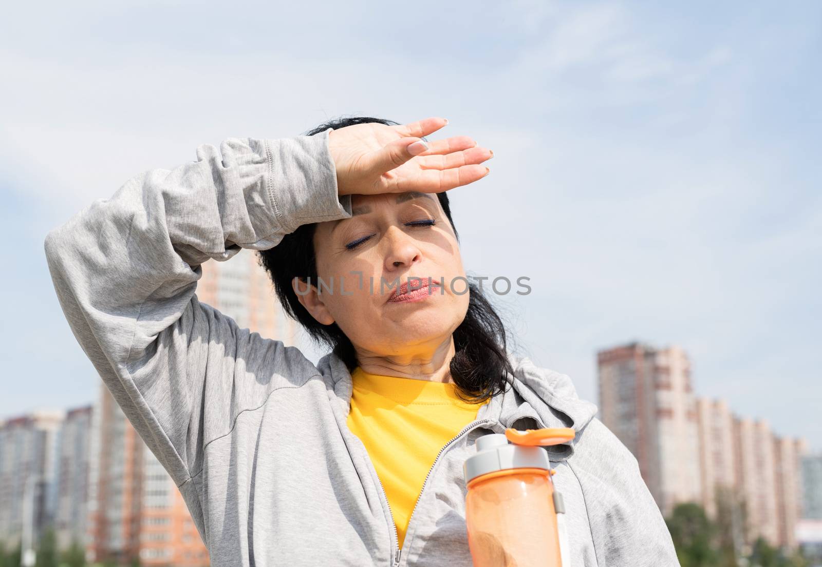 senior woman wiping out sweat after hard workout outdoors in the park by Desperada