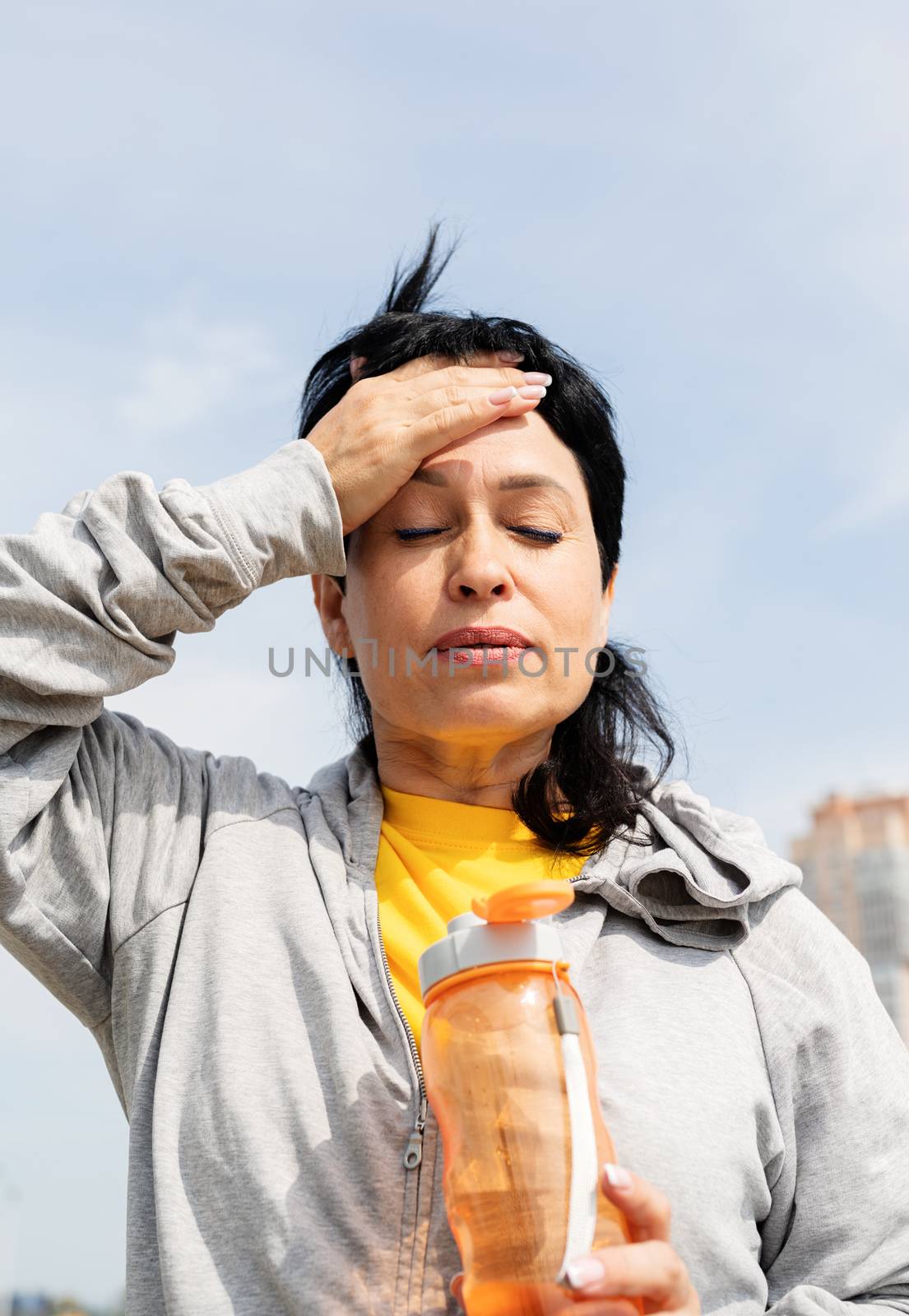 senior woman wiping out sweat after hard workout outdoors in the park by Desperada