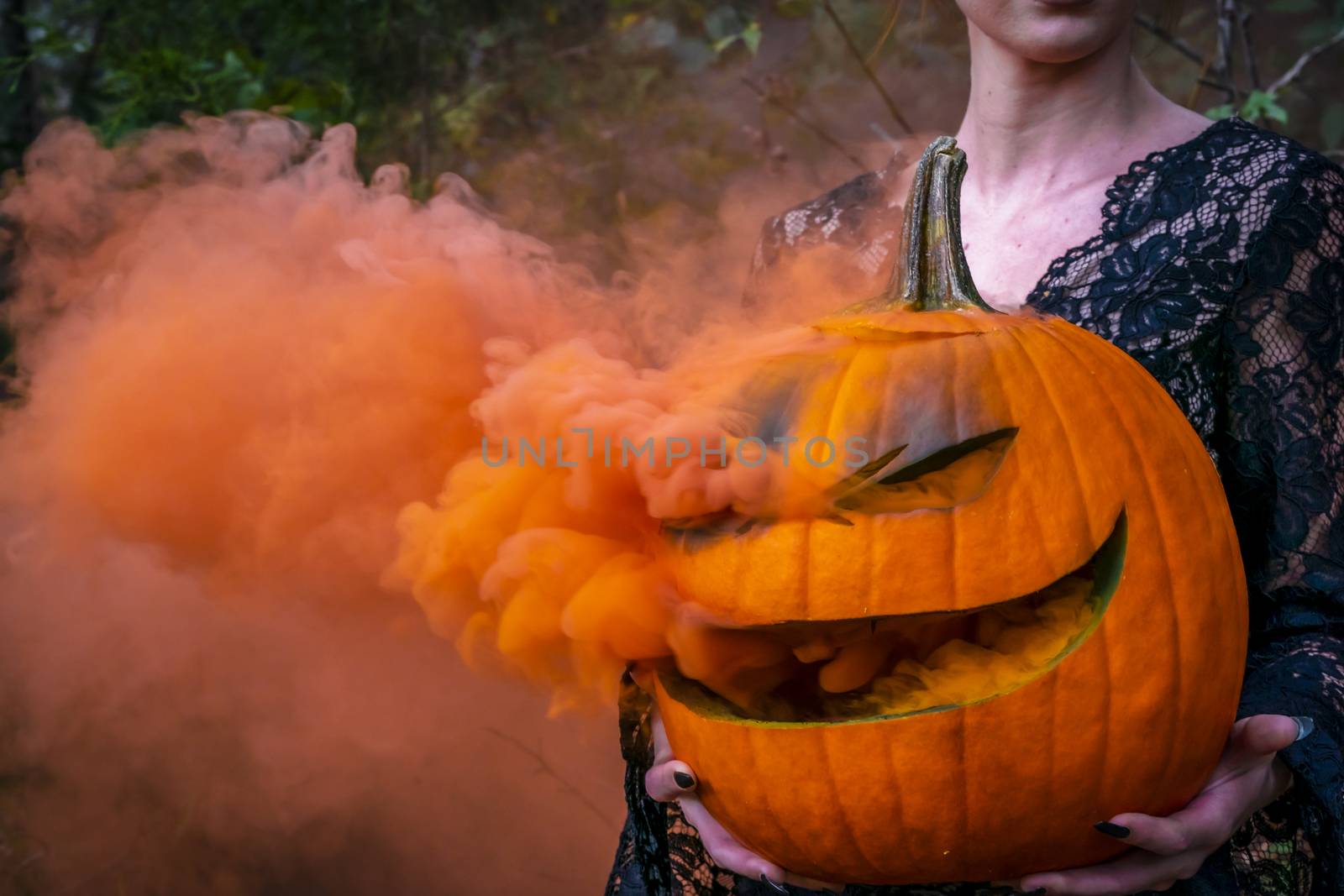 A beautiful blonde model wearing all black poses with a smoking pumpkin in an outdoor environment