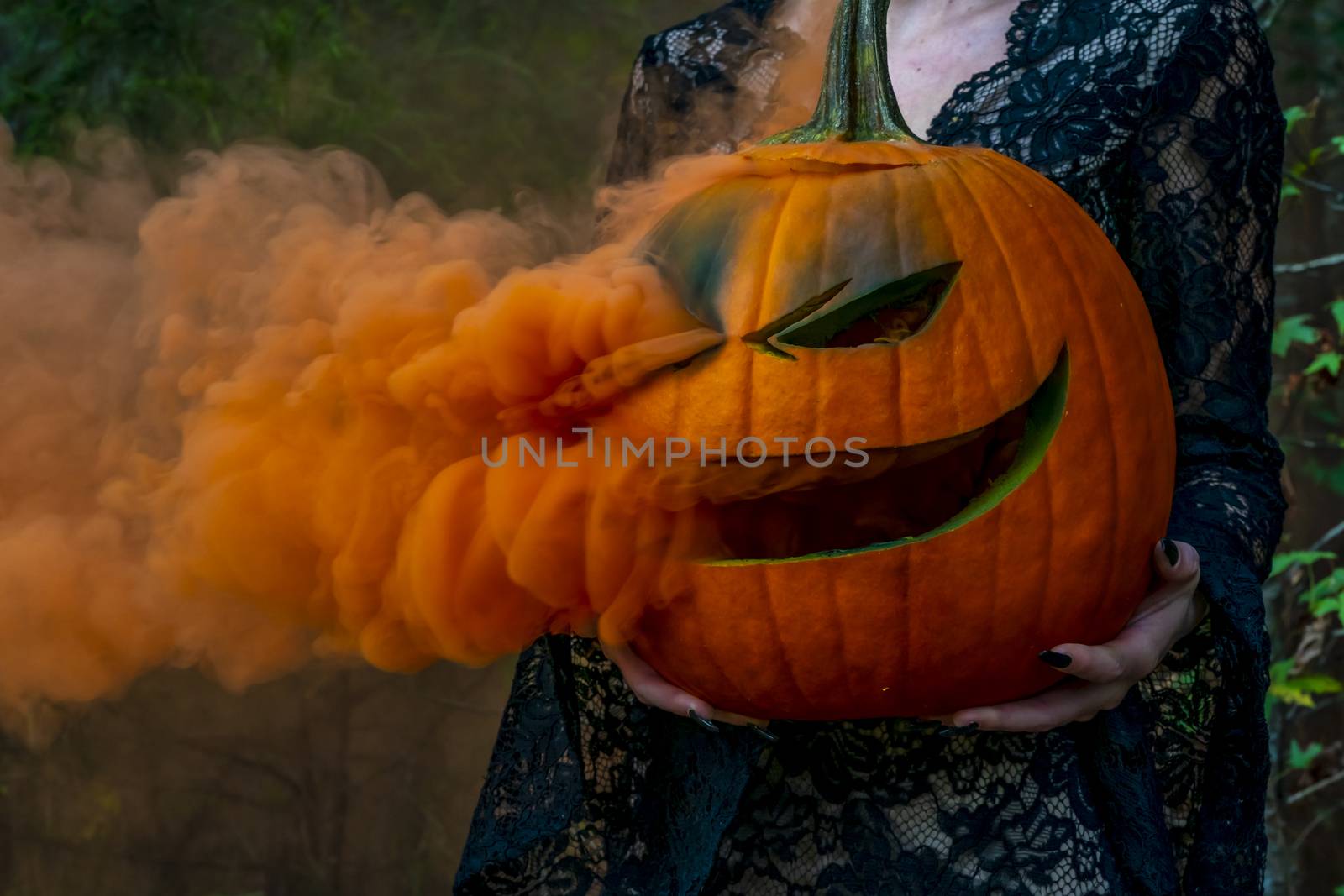 A beautiful blonde model wearing all black poses with a smoking pumpkin in an outdoor environment