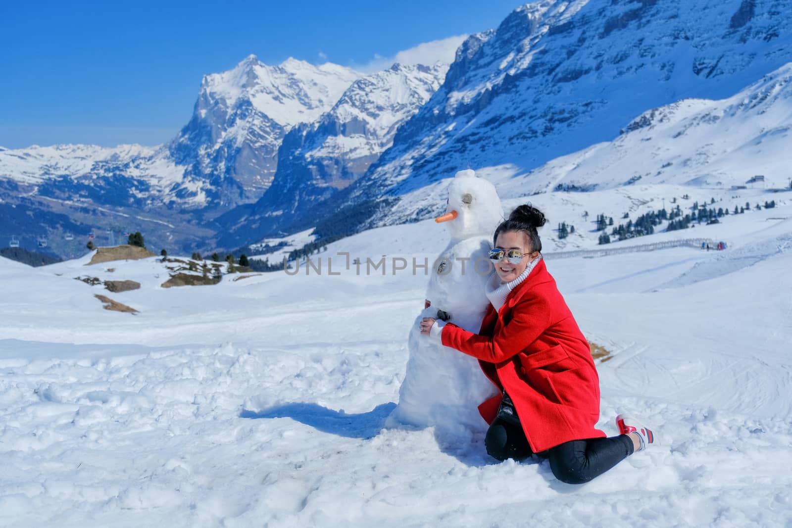 Beautiful woman hugging snowman in red coat outdoors