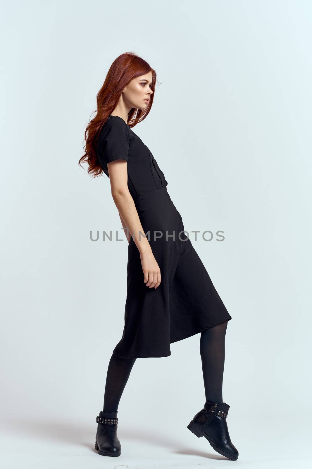 A woman in a black dress on a light background and pantyhose shoes red hair and pose in full growth by SHOTPRIME