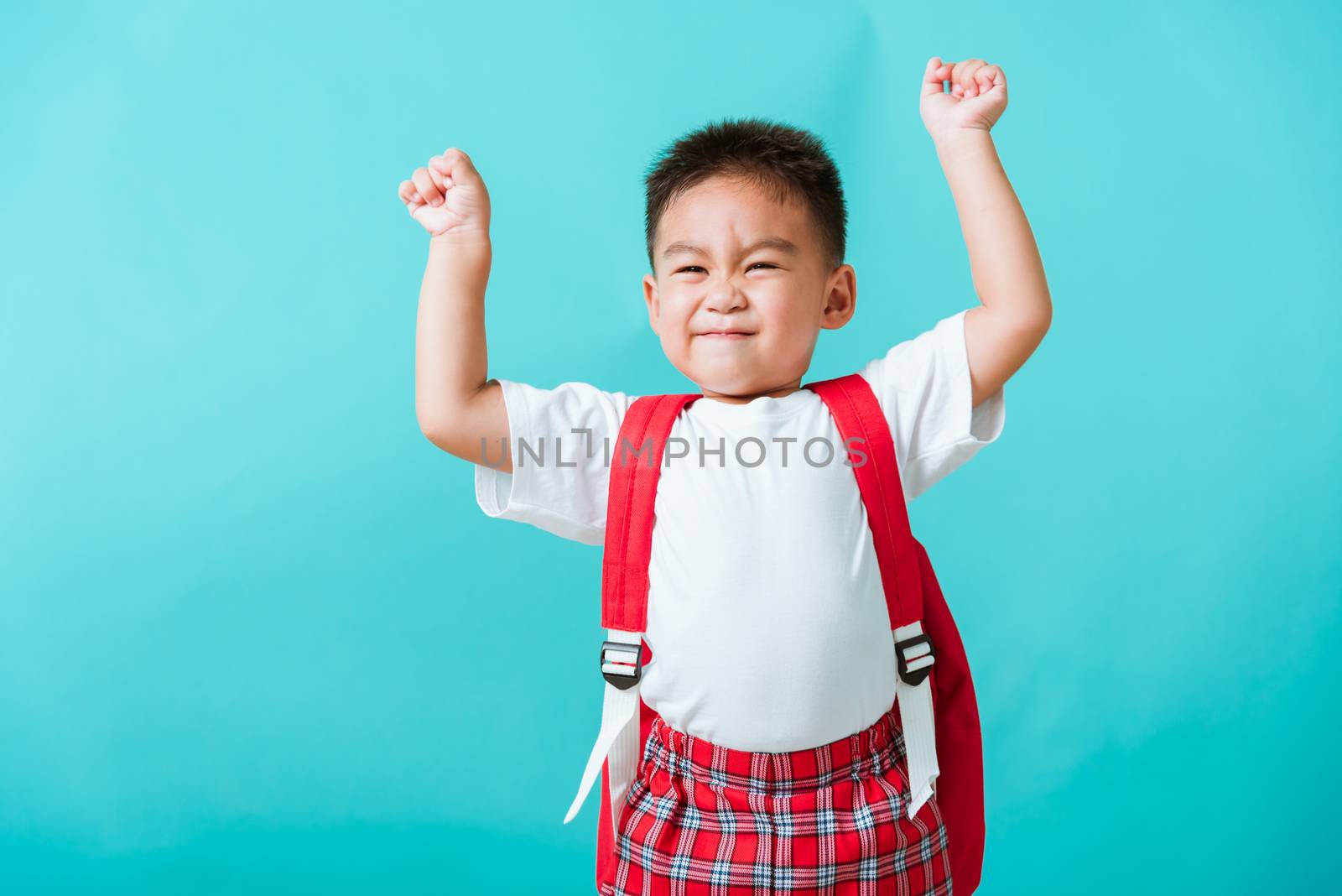 Back to school. Portrait happy Asian cute little child boy in uniform smile raise hands up glad when go back to school, isolated blue background. Kid from preschool kindergarten with school backpack