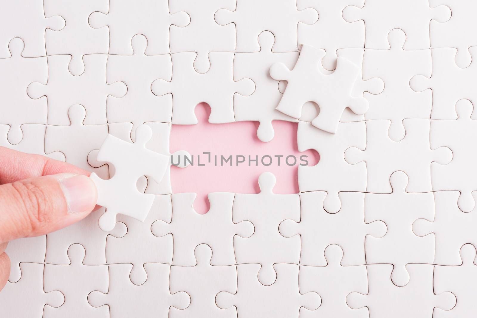 Top view flat lay of hand-holding last piece white paper jigsaw puzzle game last pieces put to place for solve problem complete mission, studio shot on a pink background, quiz calculation concept